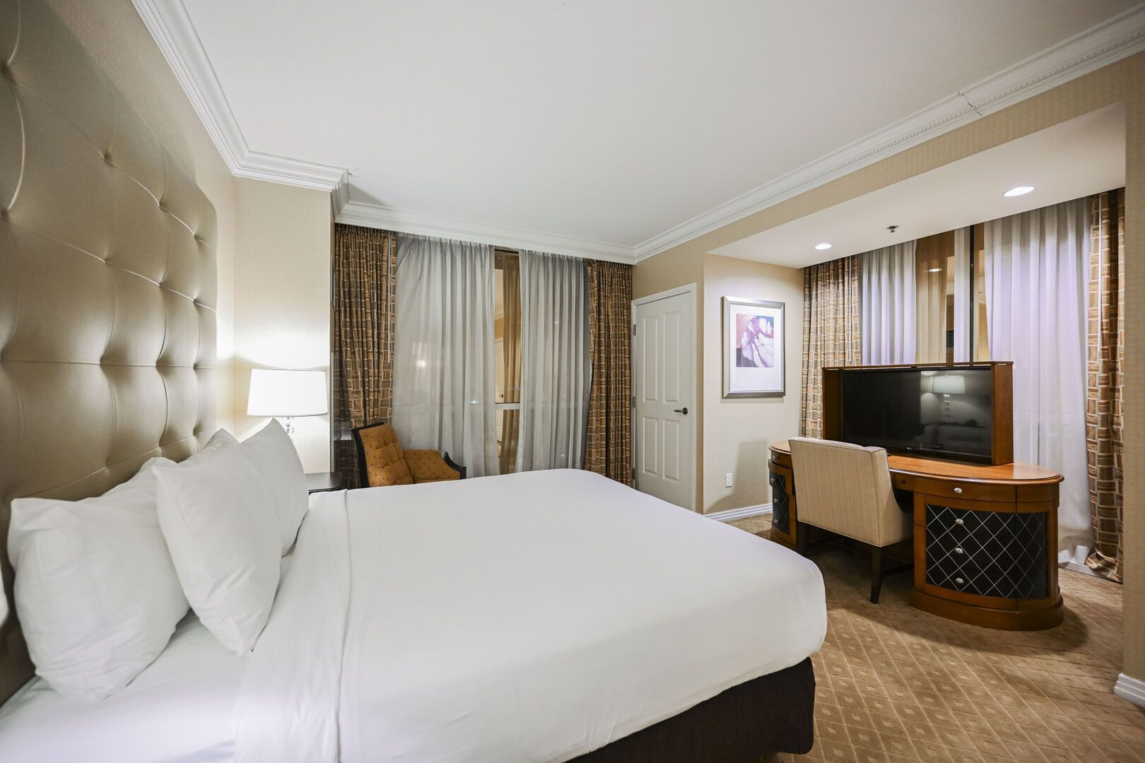 A hotel room with a large bed, a desk with a television, a chair, and a door.