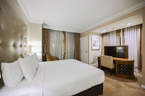 Ein Hotelzimmer mit einem großen Bett, einem Schreibtisch mit Fernseher, einem Sessel und einer Tür.