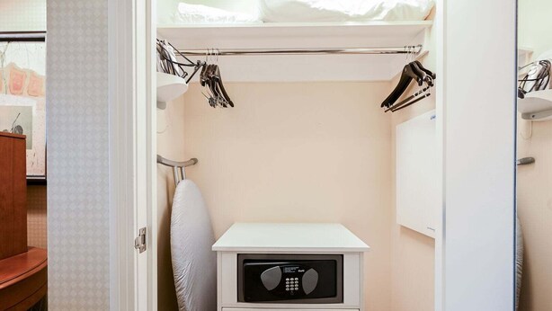 Ein kleines Zimmer mit Bett, Nachttisch, Heizung und Kleiderschrank mit Kleidung.