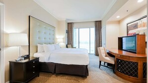 Ein Hotelzimmer mit Bett, Schreibtisch mit Fernseher, Stuhl und Nachttisch mit Lampe.