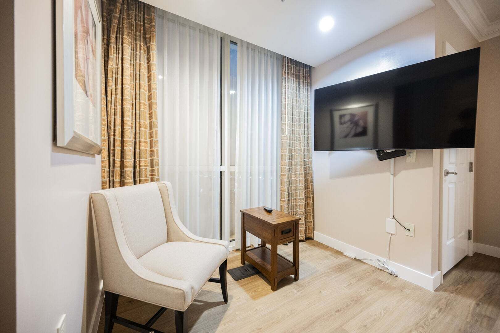Ein Zimmer mit einem Sessel, einem kleinen Tisch, einem an der Wand befestigten Fernseher und einer Tür.