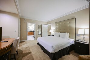 Quarto de hotel com cama, escrivaninha, cadeira, mesa de cabeceira e espelho.