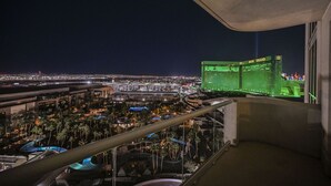 Vista noturna de uma varanda com um horizonte urbano, área de piscina e um edifício com iluminação verde.