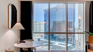 Ein Hotelzimmer mit großem Fenster, rundem Tisch, einem Sessel, einer Lampe und einer Pflanze.