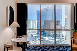Ein Hotelzimmer mit großem Fenster, rundem Tisch, einem Sessel, einer Lampe und einer Pflanze.