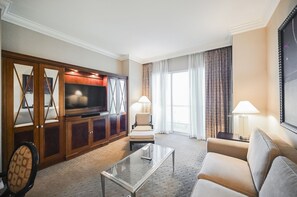 Ein Hotelzimmer mit Fernseher, einer Couch, einem Couchtisch und einem großen Fenster mit Vorhängen.