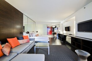 Ein modernes Hotelzimmer mit einer Couch, einem kleinen Couchtisch, einem Fernseher und einer Küchenzeile.