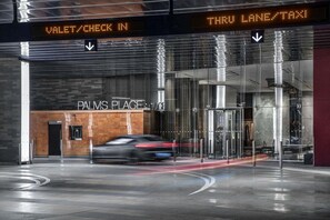 Ein moderner Gebäudeeingang mit einer digitalen Anzeige, die Valet-Service/Check-in und eine Durchfahrt für Taxis kennzeichnet.