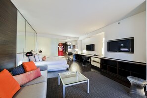 Ein modernes Hotelzimmer mit einer Couch, einem Glastisch, einem Fernseher und einer Küchenzeile.