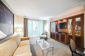 Une chambre d’hôtel équipée d’un canapé, d’un fauteuil, d’une table basse, d’une télévision et offrant une vue sur la ville.