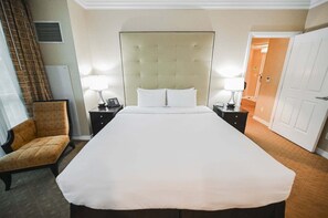 Une chambre d’hôtel avec un grand lit, deux tables de chevet avec des lampes, une chaise et une porte.