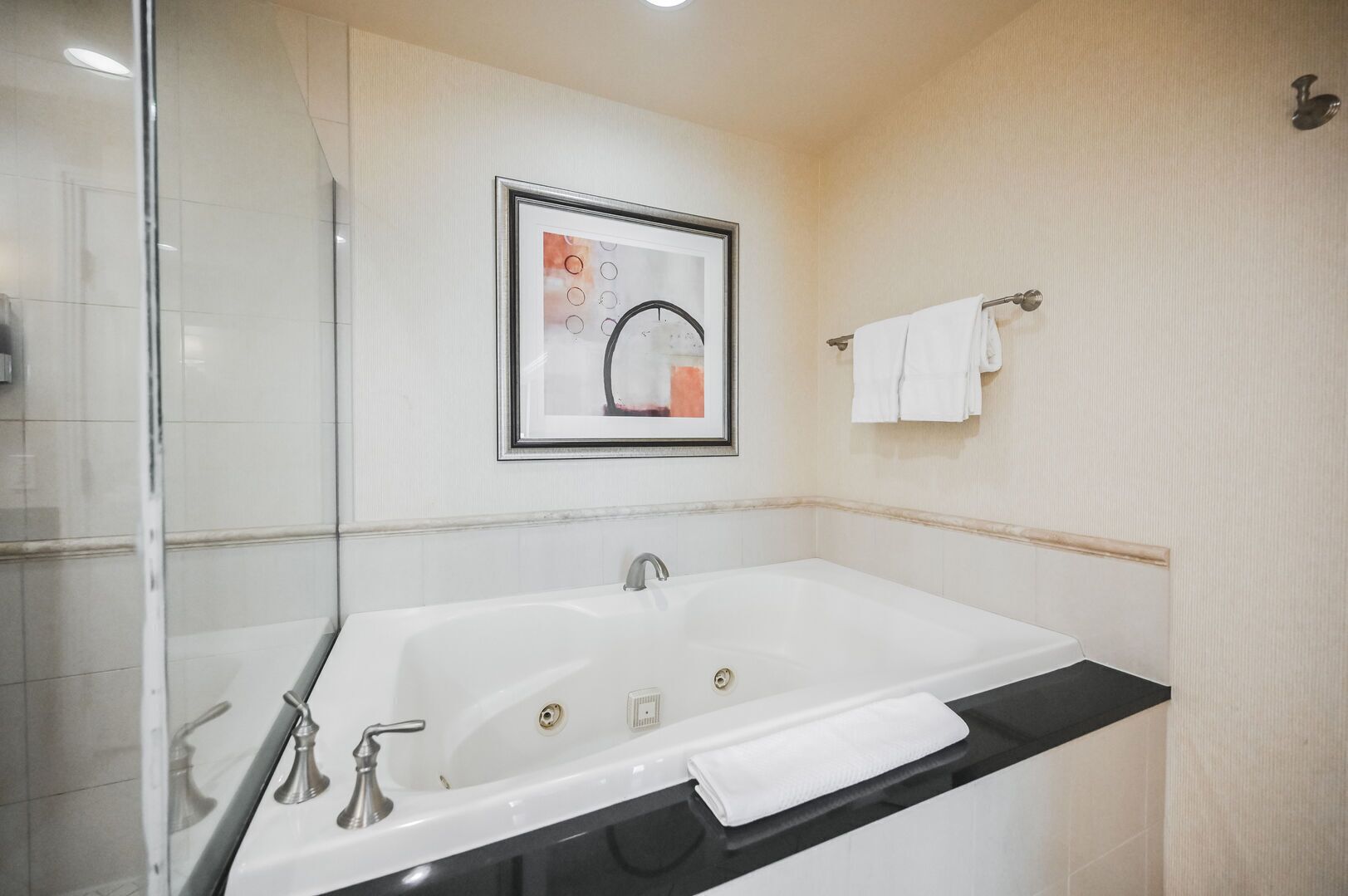 Un bagno moderno con una grande vasca, un'opera d'arte incorniciata sopra il lavabo e un portasciugamani sulla parete.