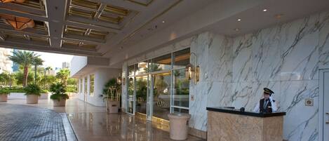 Un hall d’hôtel doté d’un comptoir de réception en marbre, d’un concierge et d’une entrée en verre.