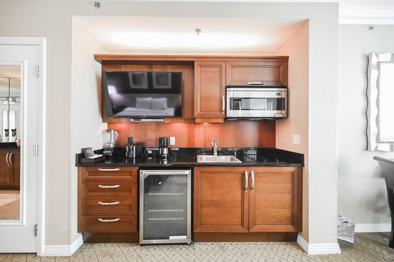 A compact kitchen with wooden cabinets, a built-in microwave, a refrigerator, and a flat-screen TV.