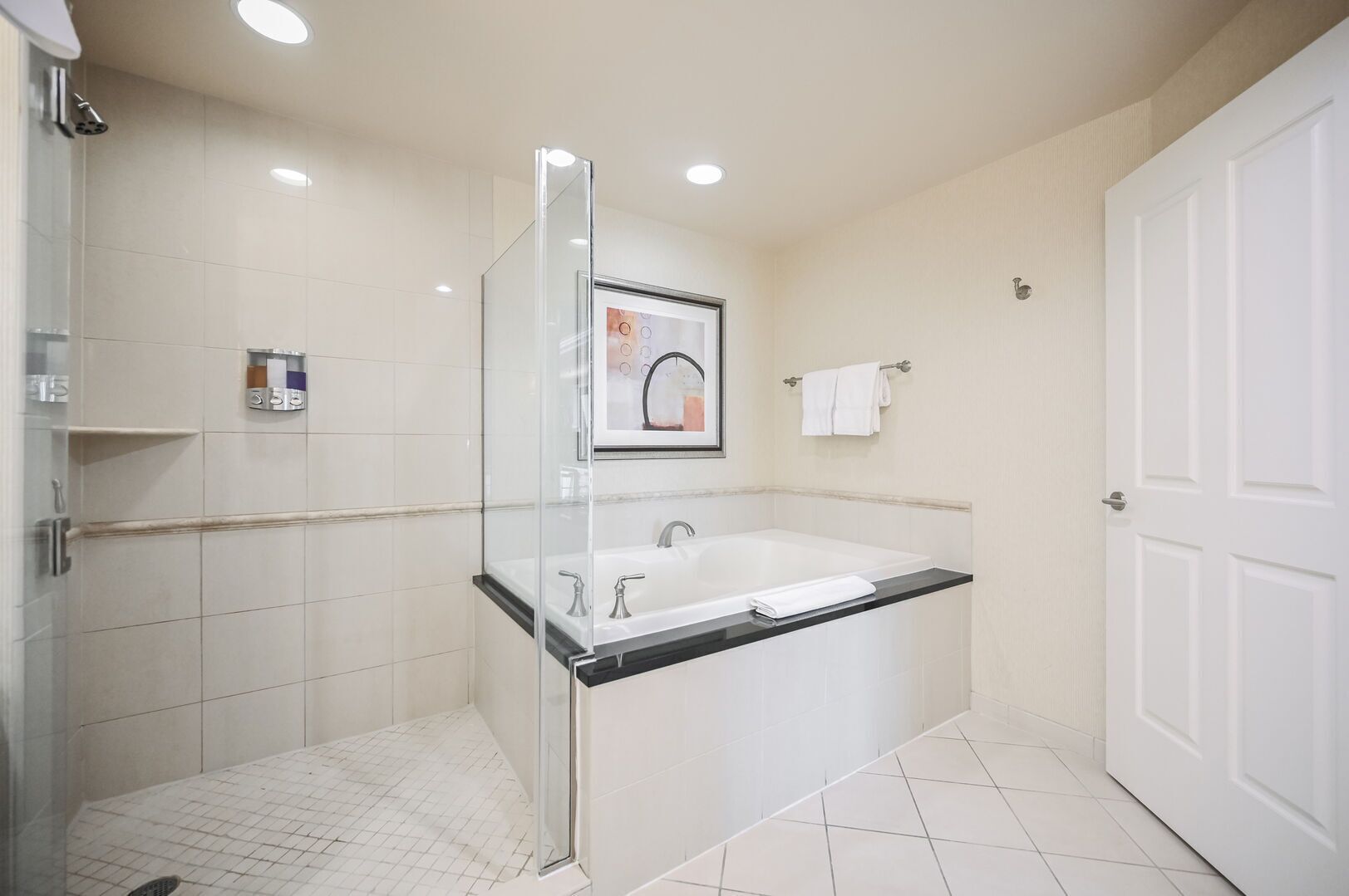 Un baño moderno con ducha de mampara de vidrio, una bañera grande y piso cubierto de baldosas blancas.