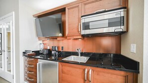 A kitchen with wooden cabinets, a stainless steel refrigerator, a black countertop, a built-in microwave, and a large flat-screen TV. - SVS: PH Floor Sphere Strip View Balcony | Signature at MGM (Las Vegas)