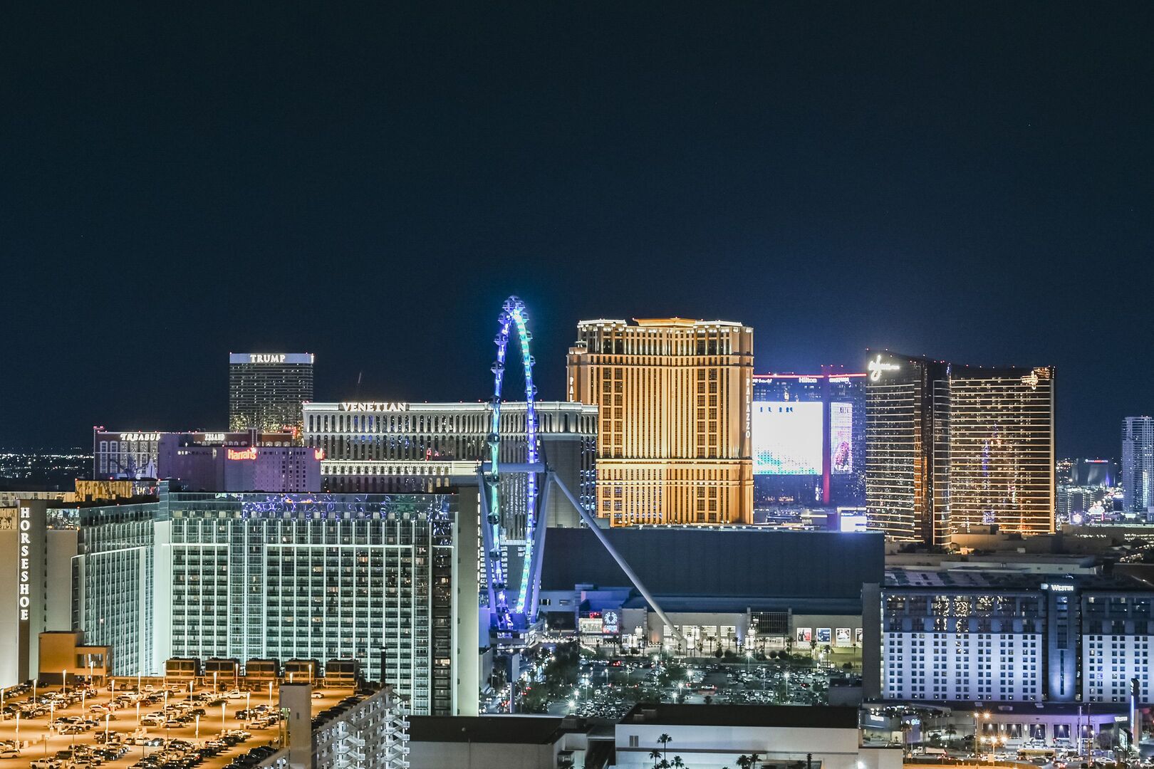 Une vue nocturne d’une ville, avec des bâtiments illuminés, dont une grande roue bien visible et plusieurs hôtels de grande hauteur.