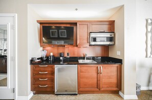 A compact kitchen with wooden cabinets, a stainless steel refrigerator, a microwave, a dishwasher, and a coffee maker. - PH Floor Studio • Strip View • Balcony • No Resort Fee D31M3 (Las Vegas)