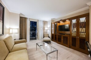 A hotel room with a sofa, a glass coffee table, a TV on a wooden cabinet, and a view of the city at night. - 1BD/2BA • Strip View • Balcony • No Resort Fee F22K3 (Las Vegas)