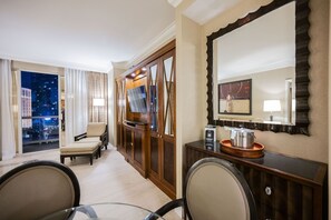 A hotel room with a large window offering a city view, a seating area with a sofa and chairs, a wooden cabinet with a flat-screen TV, and a mirror with a decorative frame. - 1BD/2BA • Strip View • Balcony • No Resort Fee F22K3 (Las Vegas)