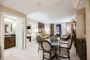 A hotel room with a dining area, a sofa, a TV, and a view of the city at night. - SVS: One Bedroom | Strip View Balcony | MGM Signature (Las Vegas)