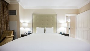 Ein Hotelzimmer mit einem großen Bett, zwei Nachttischen mit Lampen, einem Sessel und einer Tür.