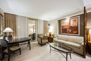 Een hotelkamer met een eettafel, twee stoelen, een bank, een glazen salontafel en een schilderij aan de muur.