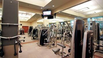 A gym with various exercise machines, a television screen, and a mirror on the wall.