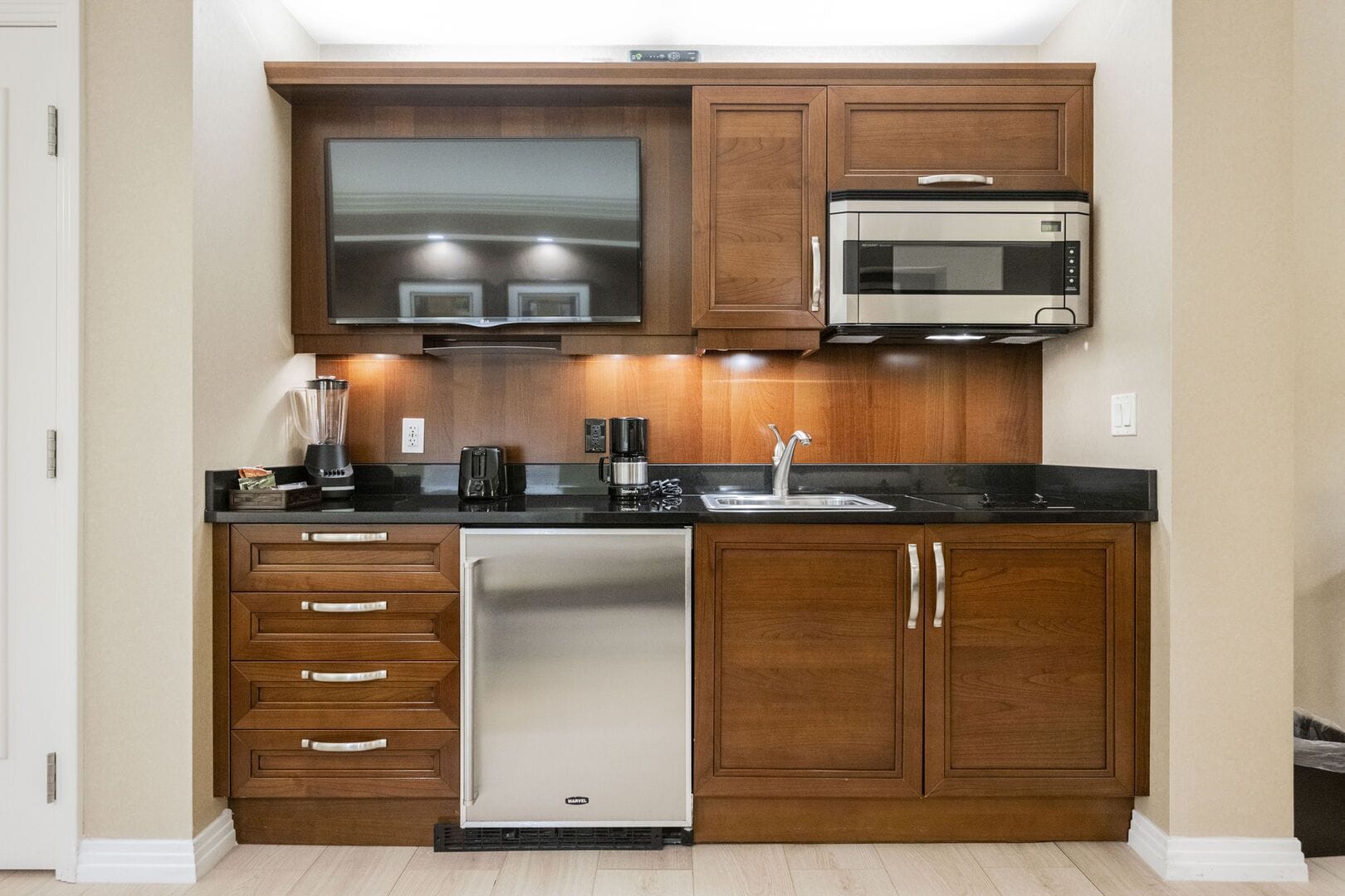 A kitchen with wooden cabinets, a built-in microwave, a dishwasher, and a flat-screen TV.