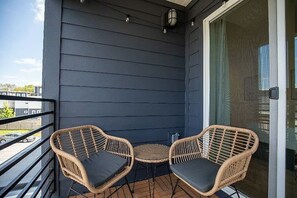 En balkon med to fletstole, et rundt bord og en skydedør, samt udsigt til en parkeringsplads.