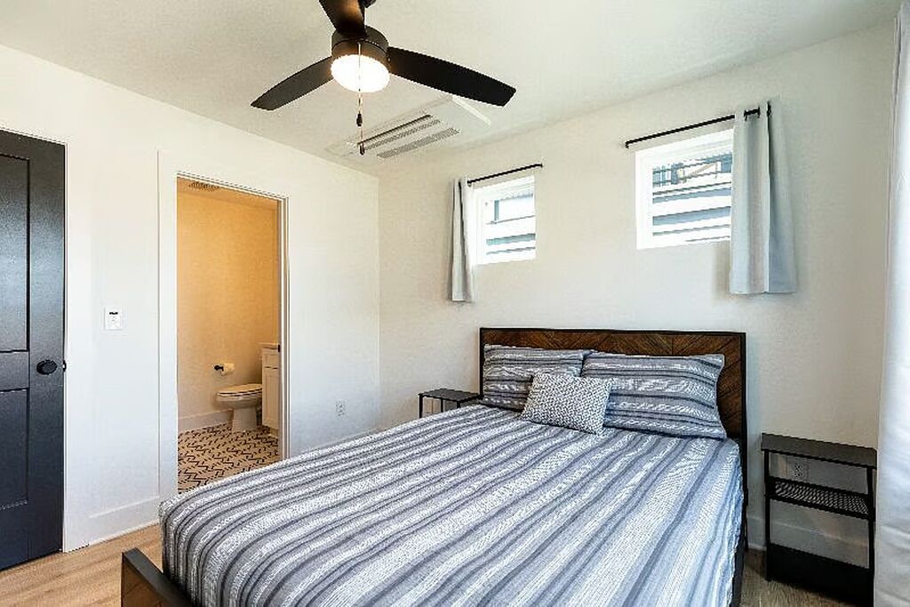 A bedroom with a bed, a ceiling fan, a window, and a door.