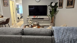 A living room with a flat-screen TV, a sofa, a coffee table, and a potted plant.