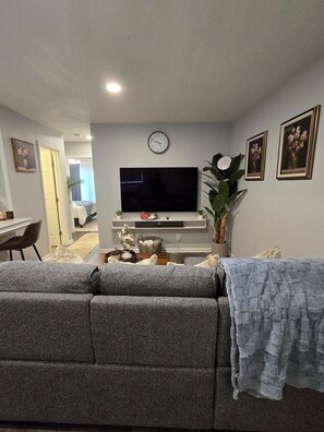 A living room with a flat-screen TV, a sofa, a coffee table, and a potted plant. - Ultra Clean 2BT w/2 Kings Near MCI and T-Mobile Center (Riverside)