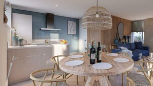 A modern kitchen with a central island, a dining area with a round wooden table, and a living area with a blue sofa. - Duinvilla Wellness 5 (De Cocksdorp)