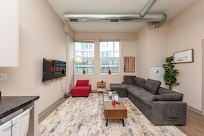 A modern living room with a sectional sofa, a flat-screen TV, a coffee table, and a patterned rug. - McCormick Modern 2BR in South Loop w/ Gym & Patio (Chicago)