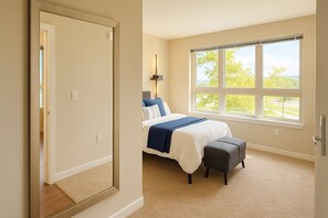 A bedroom with a bed, a bench, a window with a view, and a door.