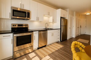 Une cuisine moderne dotée d’appareils électroménagers en acier inoxydable, de meubles blancs et d’une chaise jaune.