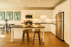Una cocina moderna con armarios blancos, electrodomésticos de acero inoxidable, una isla central con taburetes y cuadros en la pared.