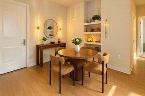 Un coin repas comprenant une table ronde en bois, six chaises, un vase avec des fleurs, un miroir et des étagères ornées d’objets décoratifs.