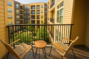 Un balcon avec des fauteuils en osier et une petite table, donnant sur une cour intérieure bordée de bâtiments.