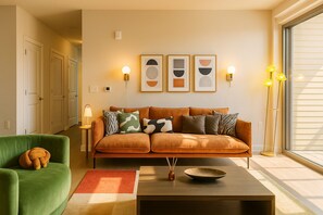 Een woonkamer met een bank, een groene fauteuil, een salontafel, een vloerlamp en wanddecoratie.