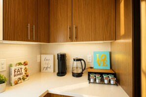 Een keuken met houten kastjes, een koffiezetapparaat, een waterkoker, een koffiemok, een lijst en een plank met potten.