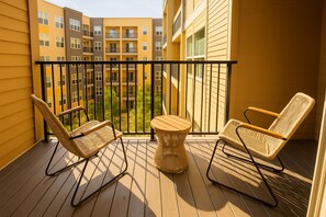 Een balkon met twee rieten stoelen en een klein, rond tafeltje, met uitzicht op een meerlaags gebouw met balkons.