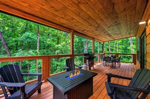 Une terrasse couverte avec des fauteuils Adirondack, un barbecue et un foyer extérieur.