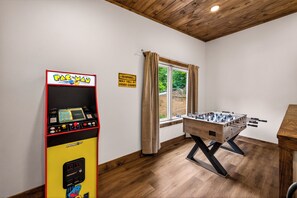 Une pièce avec un baby-foot, une borne d’arcade Pac-Man et une fenêtre avec des rideaux.