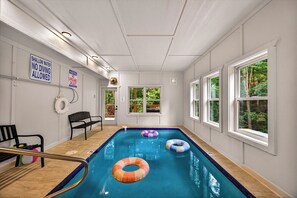 Une piscine intérieure avec un panneau indiquant une faible profondeur, un avertissement indiquant la présence d’un sauveteur et une vue sur les arbres à travers les fenêtres.