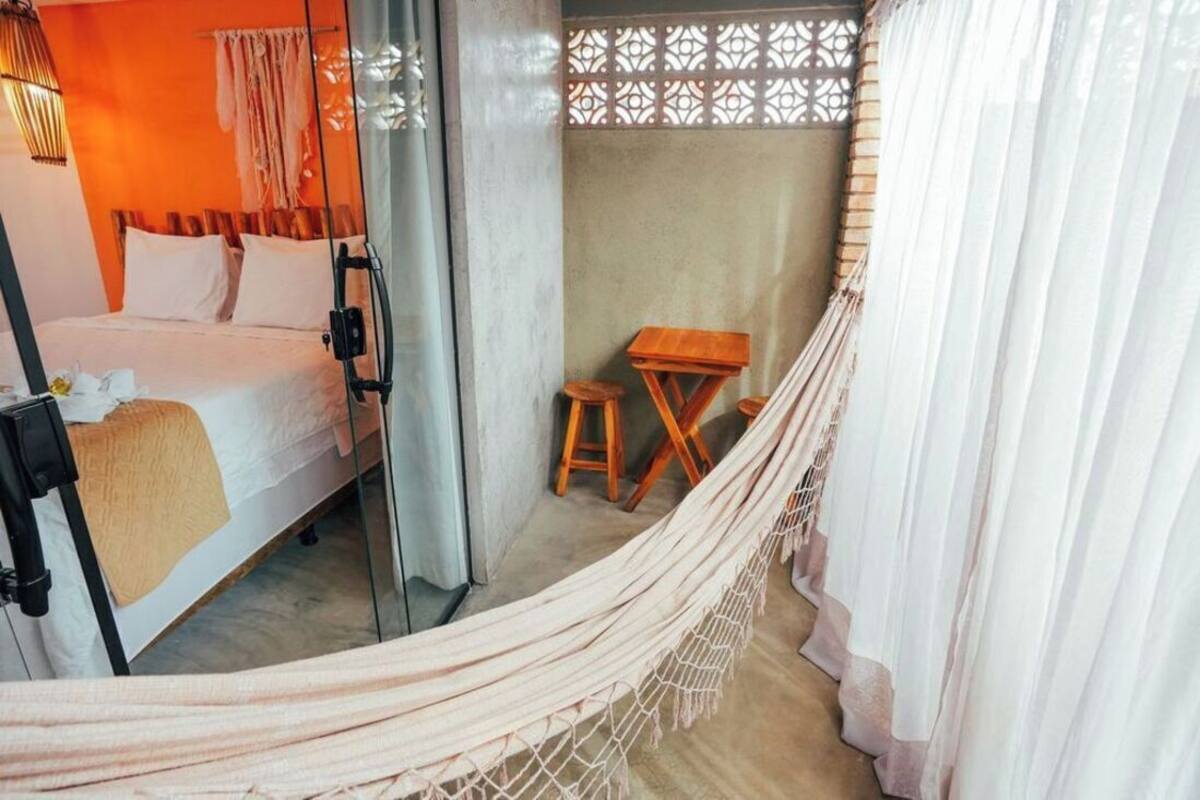 A room with a bed, a small wooden table, a hammock, and a partition with a lattice design.