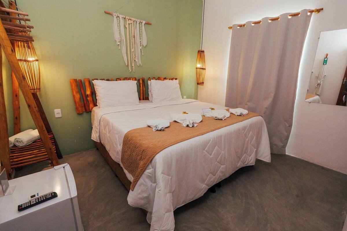 A neatly made bed with white and brown linens, a wooden ladder, a wall-mounted light fixture, and a mirror with a curtain.