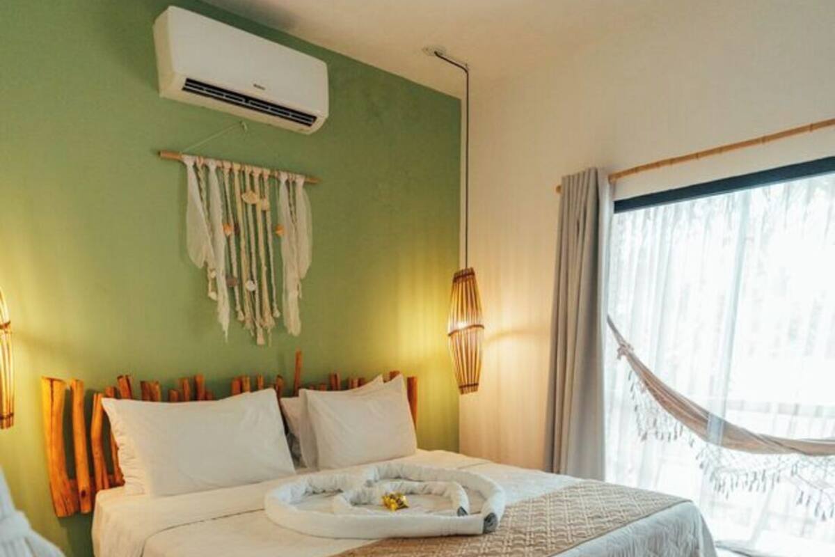 A bedroom with a bed, a hanging light fixture, a window with curtains, and a wall-mounted air conditioner.