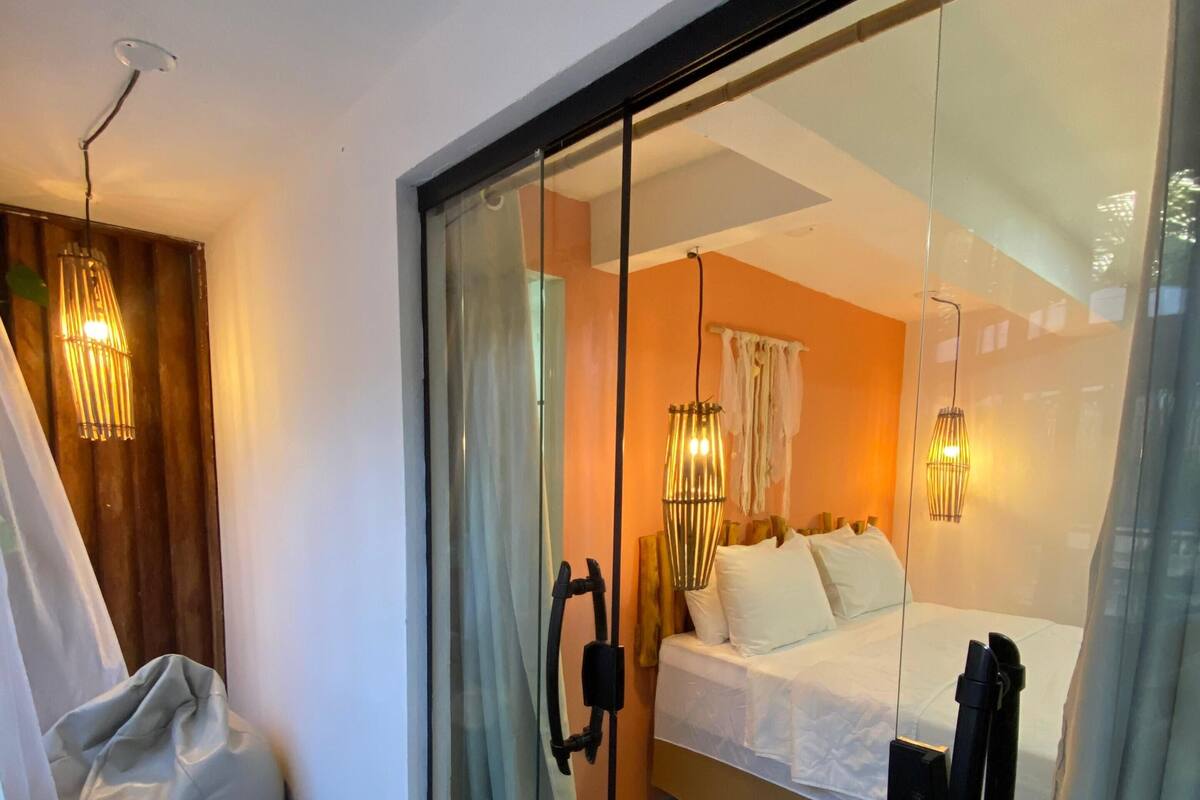 A modern bedroom with a glass door, a bean bag, a bed, and pendant lights.